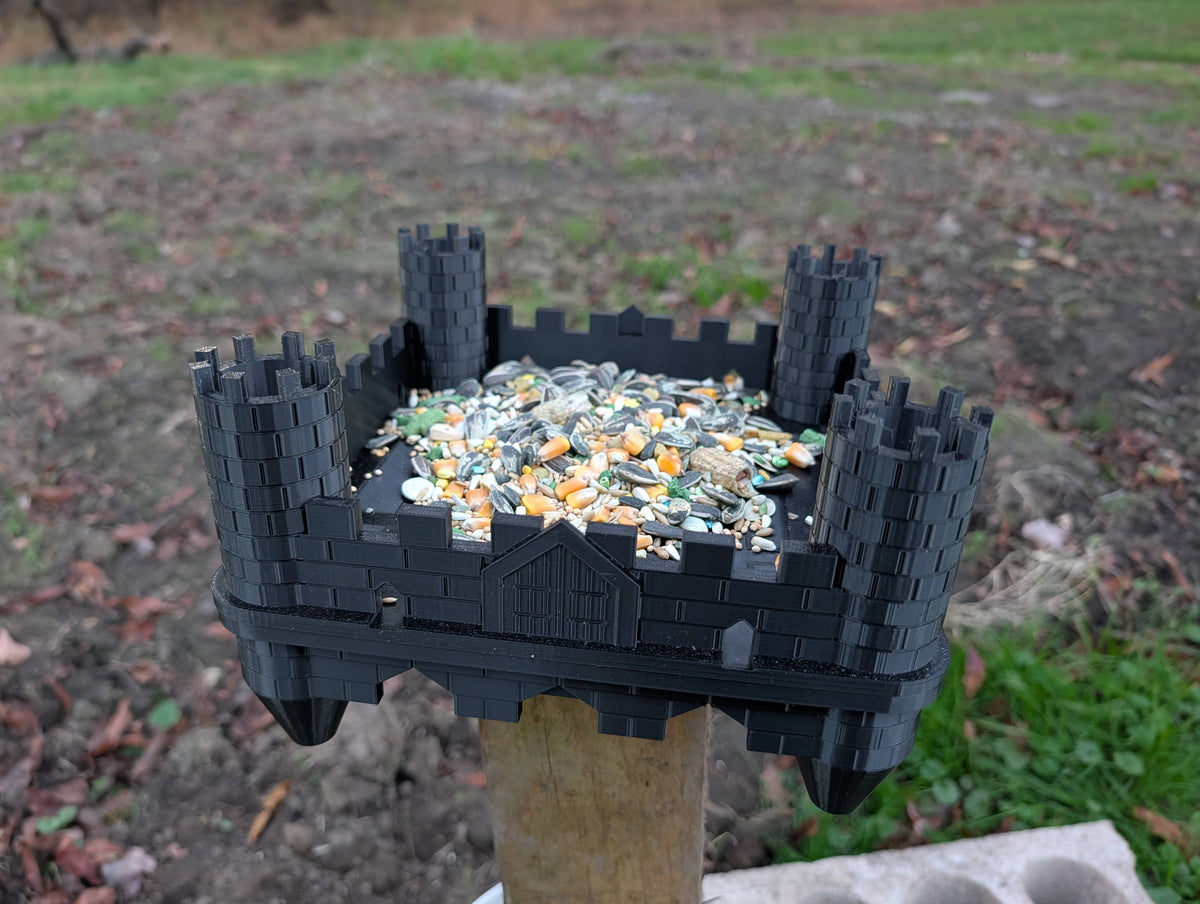 Black castle bird feeder installed on a wooden post with birdseed; post and seed not included