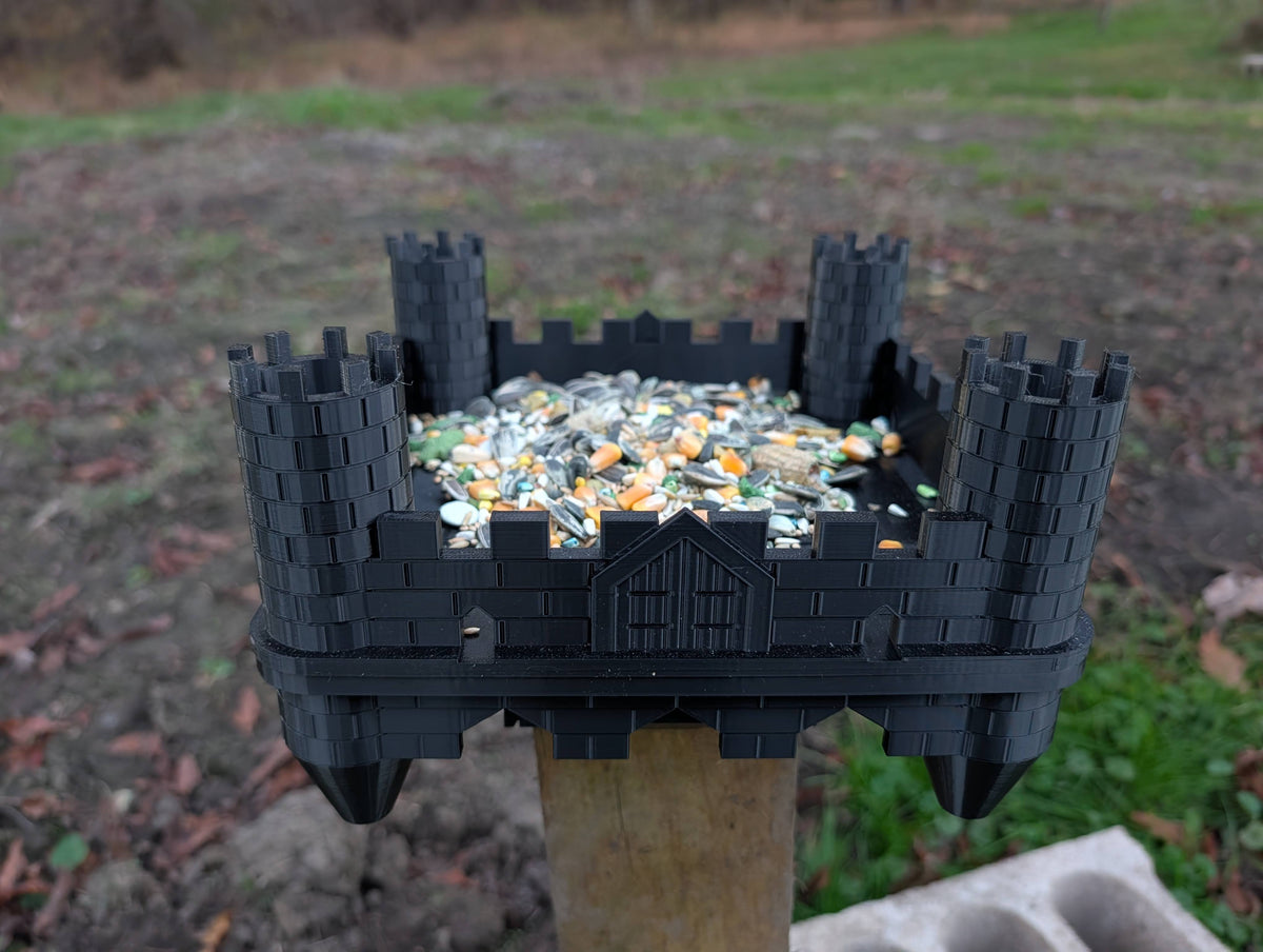 Black castle bird feeder installed on a wooden post with birdseed; post and seed not included