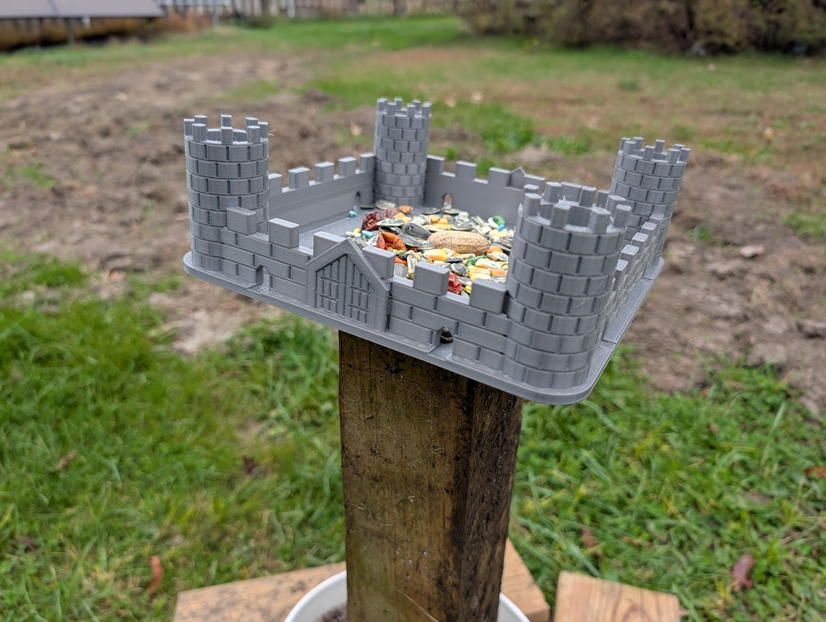 Front view of grey castle bird feeder showing four towers and a decorative gate