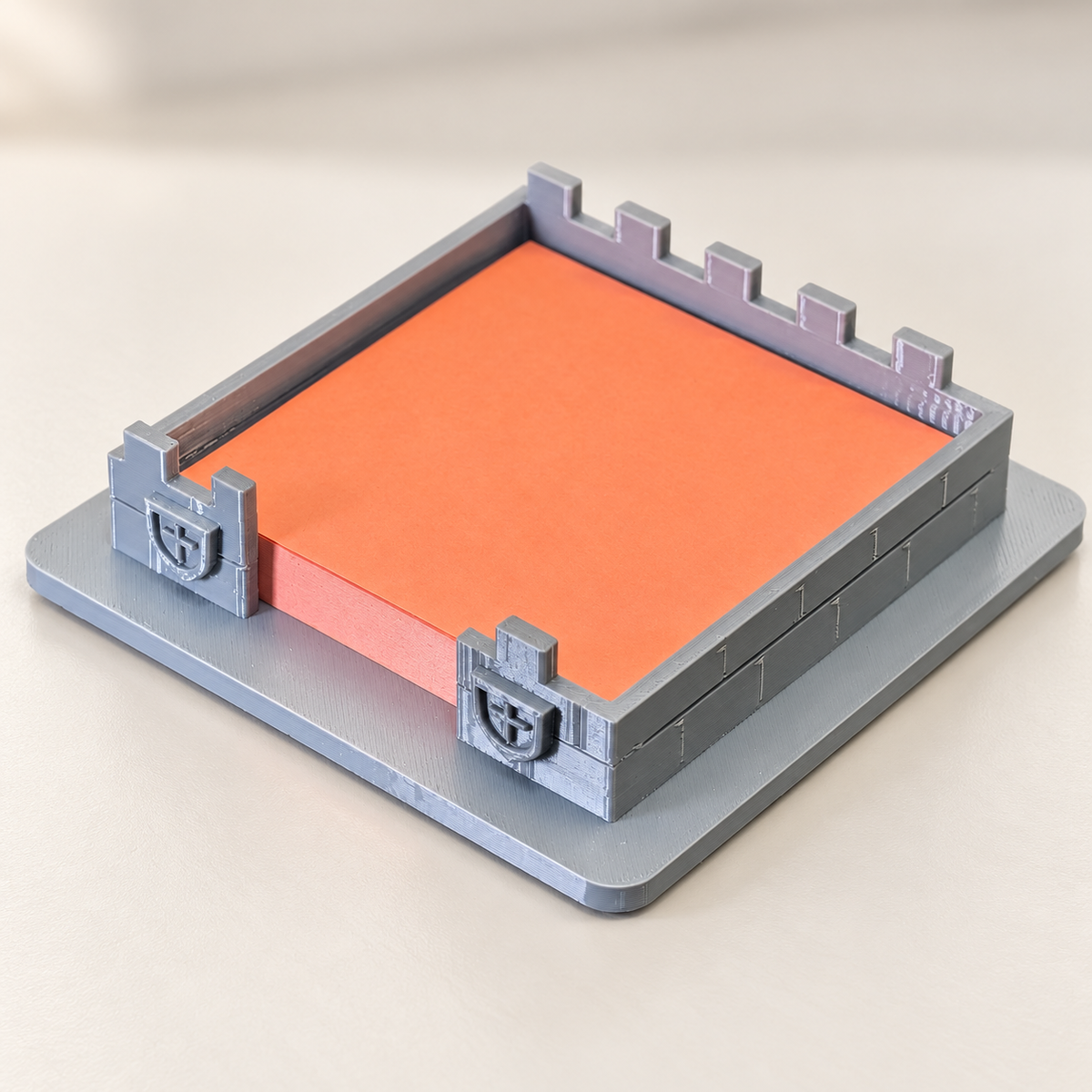 Grey castle sticky-note holder with orange pad, shields and battlements